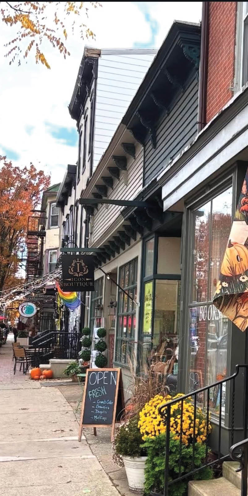 A person is holding a cup of coffee with a leaf design in the foam outside a coffee shop decorated with pumpkins and flowers. Description generated by AI