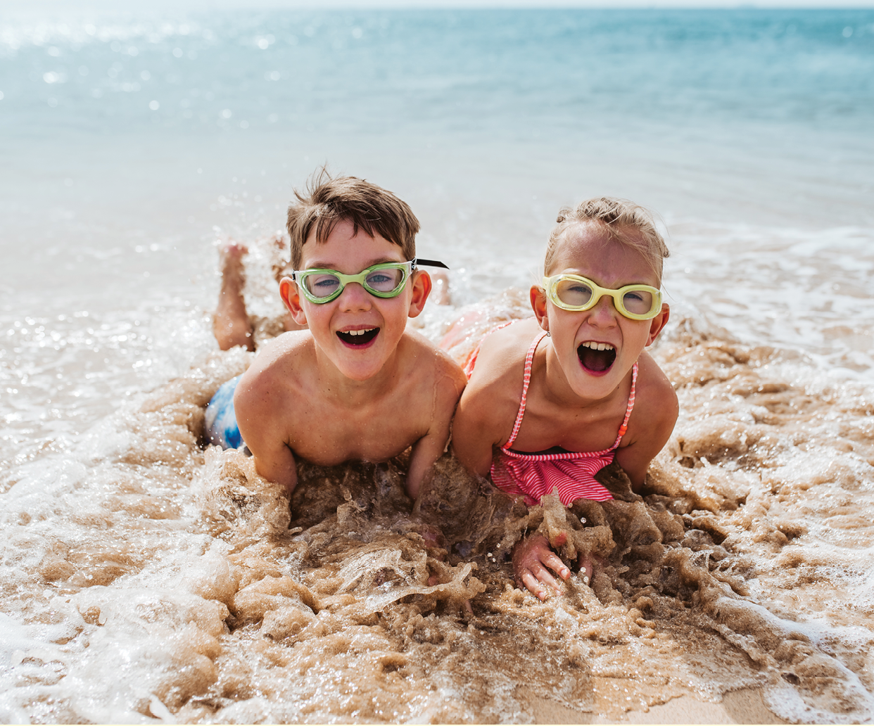 Siblings playing on beach, running, having fun. Smilling girl and boy on sandy beach with vulcanic rocks of Canary islands. Concept of a family beach summer vacation with kids.