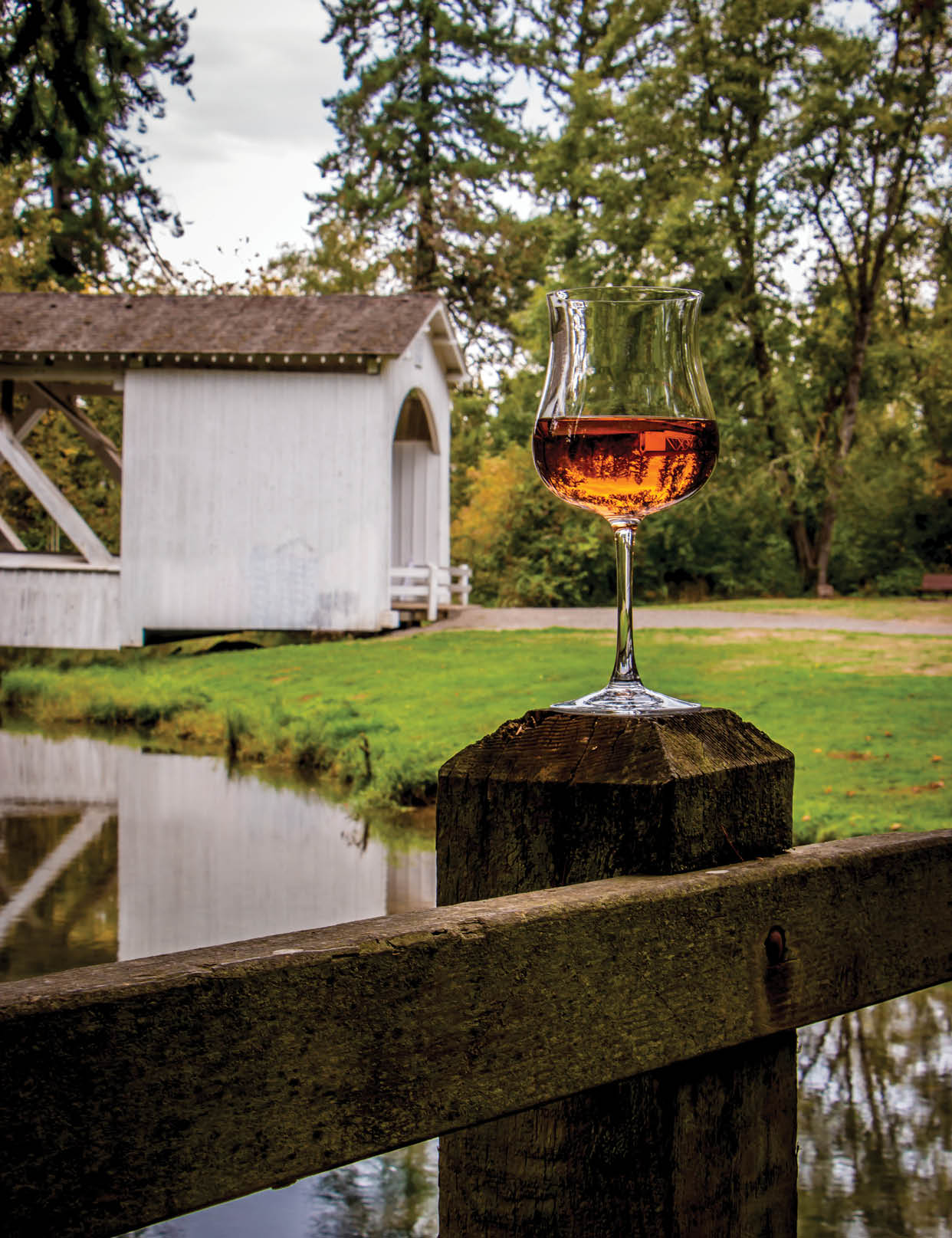 Unique shaped Wine glass featuring Ros Wiine. Oregon's Willamette Valley.  Inverted image of the Covered Bridge in Stayton spanning Thomas Creek, seen while on a driving tour of Linn County Covered Bridges. Also known as the Thomas Creek Bridge. Serene setting in a park.  Still waters in Creek reflecting the bridge and trees. Artistic and Illustrative. Vertical. No people, nobody.