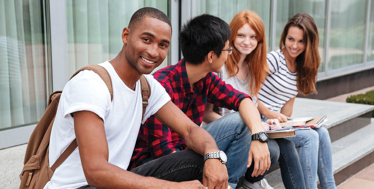 Happy african american young man student sitting with his frieds outdoors