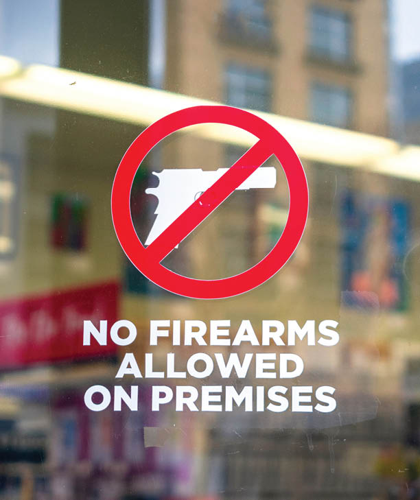 No firearms allowed on premises sign on the glass entrance door to establishment notifies patrons that weapons aren't allowed, addresses security policy and protection concerns.