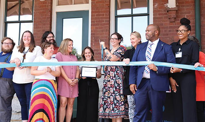 A group of people are standing in front of a building, posing for a picture. They are all wearing name tags, and there is a ribbon in front of them. AI generated content