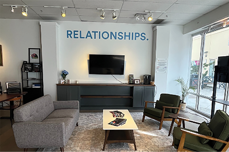 A living room with a couch, chair, and coffee table. A flat screen TV is mounted on the wall above the table. A sign on the wall reads “Relationships." AI generated content