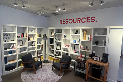 A room with a white shelf and a sign that says “Resources." A rug is on the floor and there are two chairs in the room. AI generated content