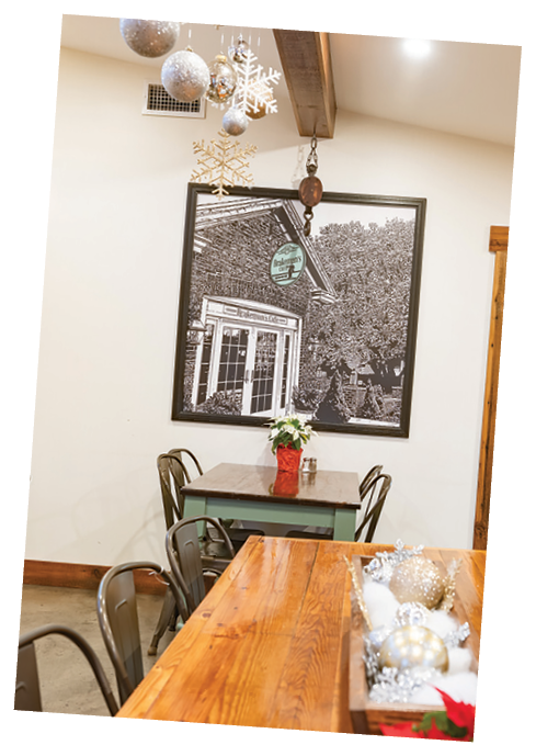 A restaurant with a wooden table and chairs. The table is set with a vase of flowers and a bowl of ornaments. The room is decorated with Christmas ornaments and a painting of a house. AI generated content