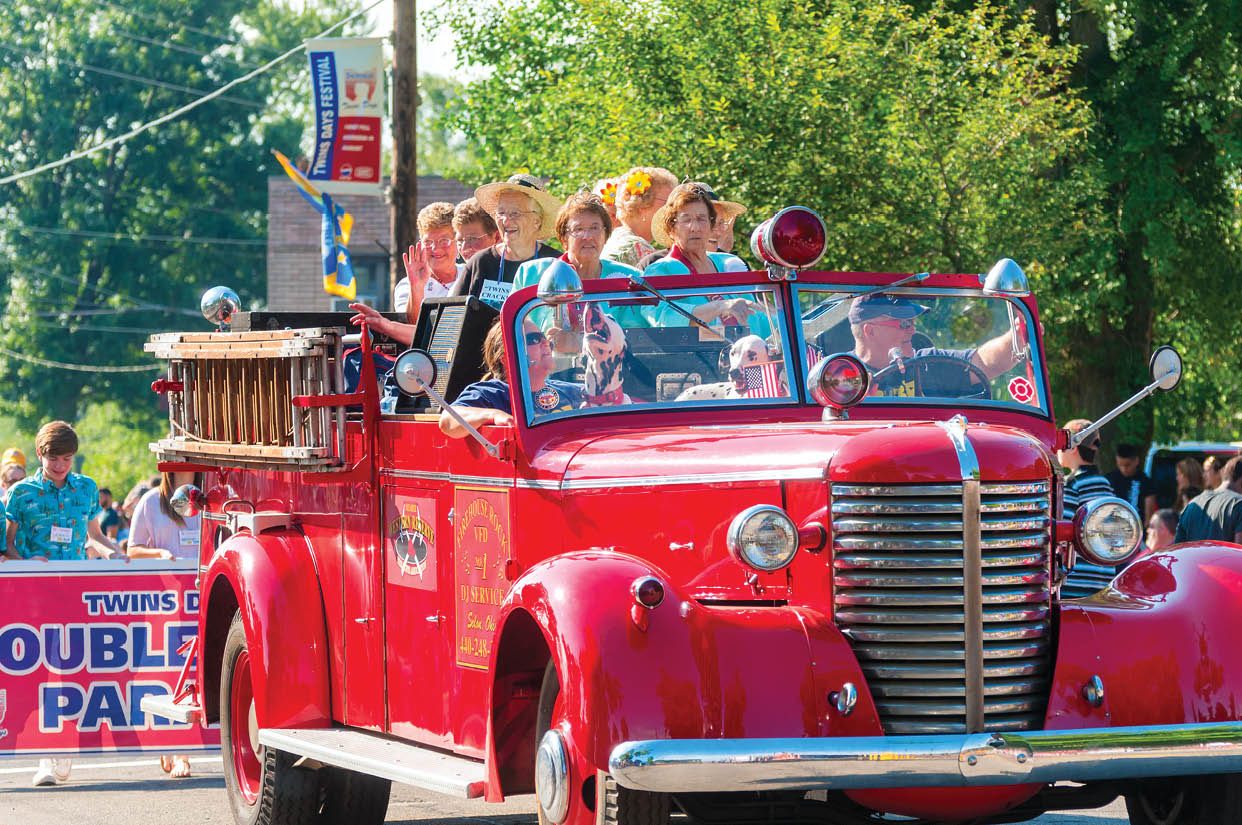 Twinsburg, OH, USA - August 8, 2015: Elderly twins ride in an old-fashioned fire truck in the Double Take Parade, part of the 40th annual Twins Day festival, the largest gathering of twins in the world.