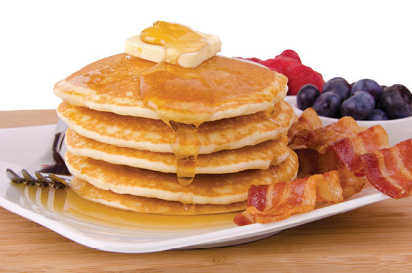 Stack of pancakes and bacon with fruits on background. Front view.