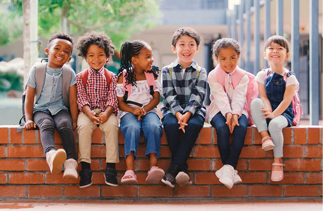 A group of children sitting on a brick wall. Description generated by AI