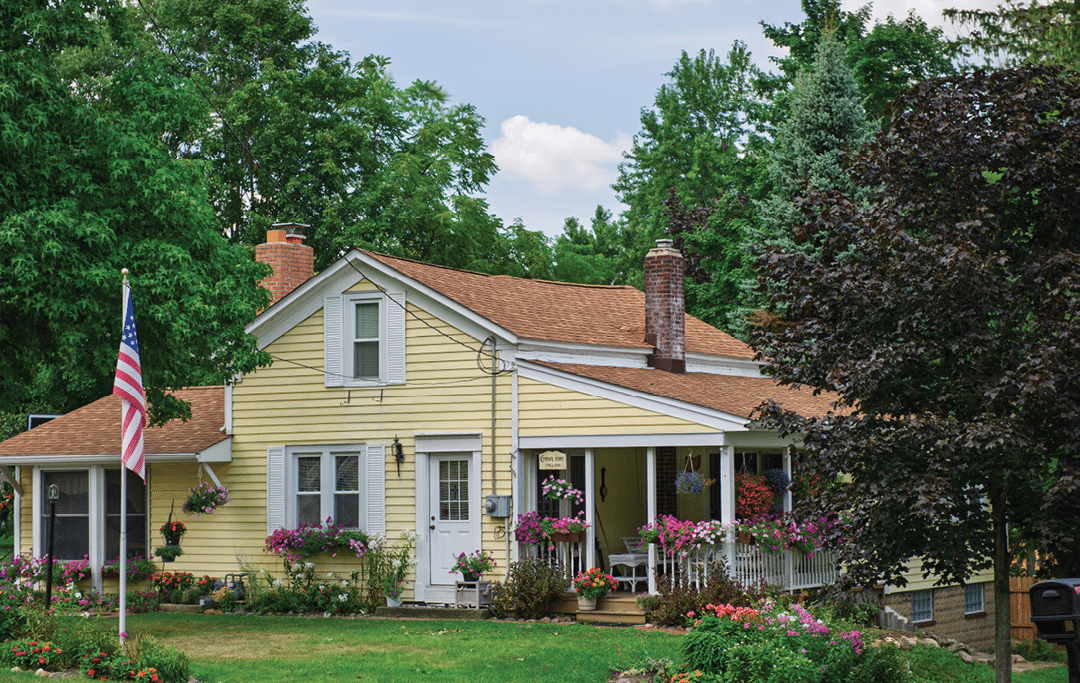A yellow house with a flag on the lawn. Description generated by AI