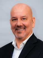 A man wearing a black suit and white shirt smiling. Description generated by AI