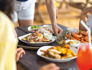 Happy Asian family couple and little kids travel ocean on summer holiday vacation. Waitress serving food and drink to customers on the table at beach restaurant at tropical island beach in sunny day.