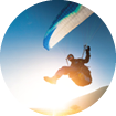 A paraglider takes off from a mountainside with a blue and white canopy and the sun behind. A paraglider is a silhouette. The glider is sharp, with little wing movement. A male paraglider launches a paraglider into the air.