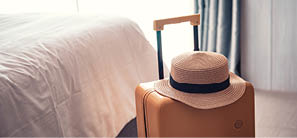 Suitcase or luggage bag with hat in a modern hotel room - relaxing time, holidays, weekend and traveling concept.
