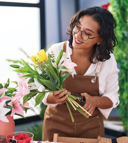 Young beautiful hispanic woman florist make bouquet of flowers at flower shop