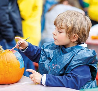 Happy little kid boy on a harvest festival, painting with colors a pumpkin. Child celebrating traditional festival halloween or thanksgiving.