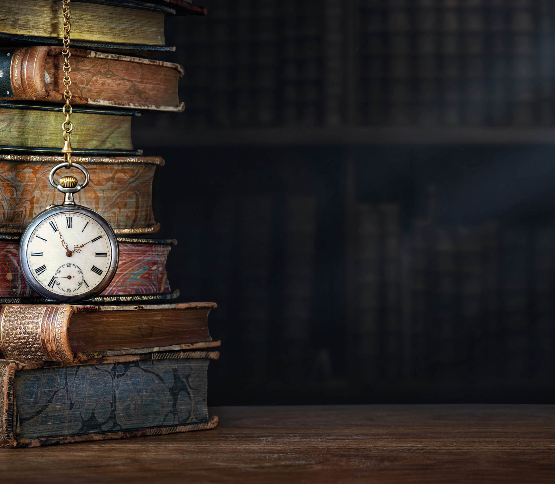 Old clock hanging on a chain on the background of old books. lock as a symbol of time a books are a symbol of knowledge.. Concept on the theme of history, nostalgia, culture.