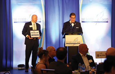 Two men standing on stage holding awards. Description generated by AI