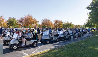 A row of golf carts parked in a parking lot. Description generated by AI