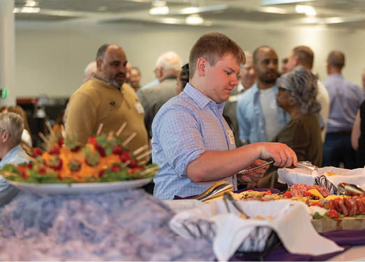 A man in a blue shirt is serving food at a buffet. Description generated by AI