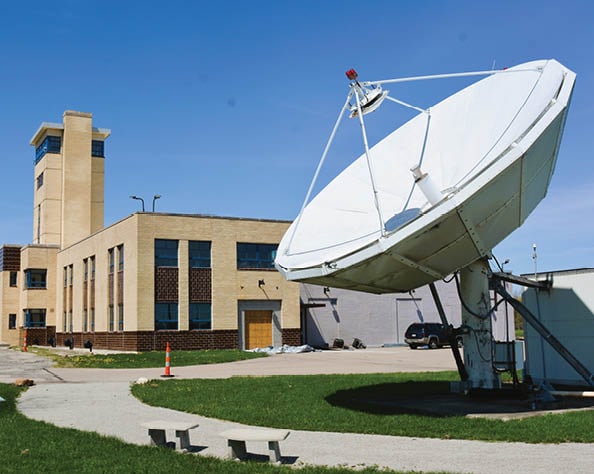 A large satellite dish is located in front of a building. AI generated content