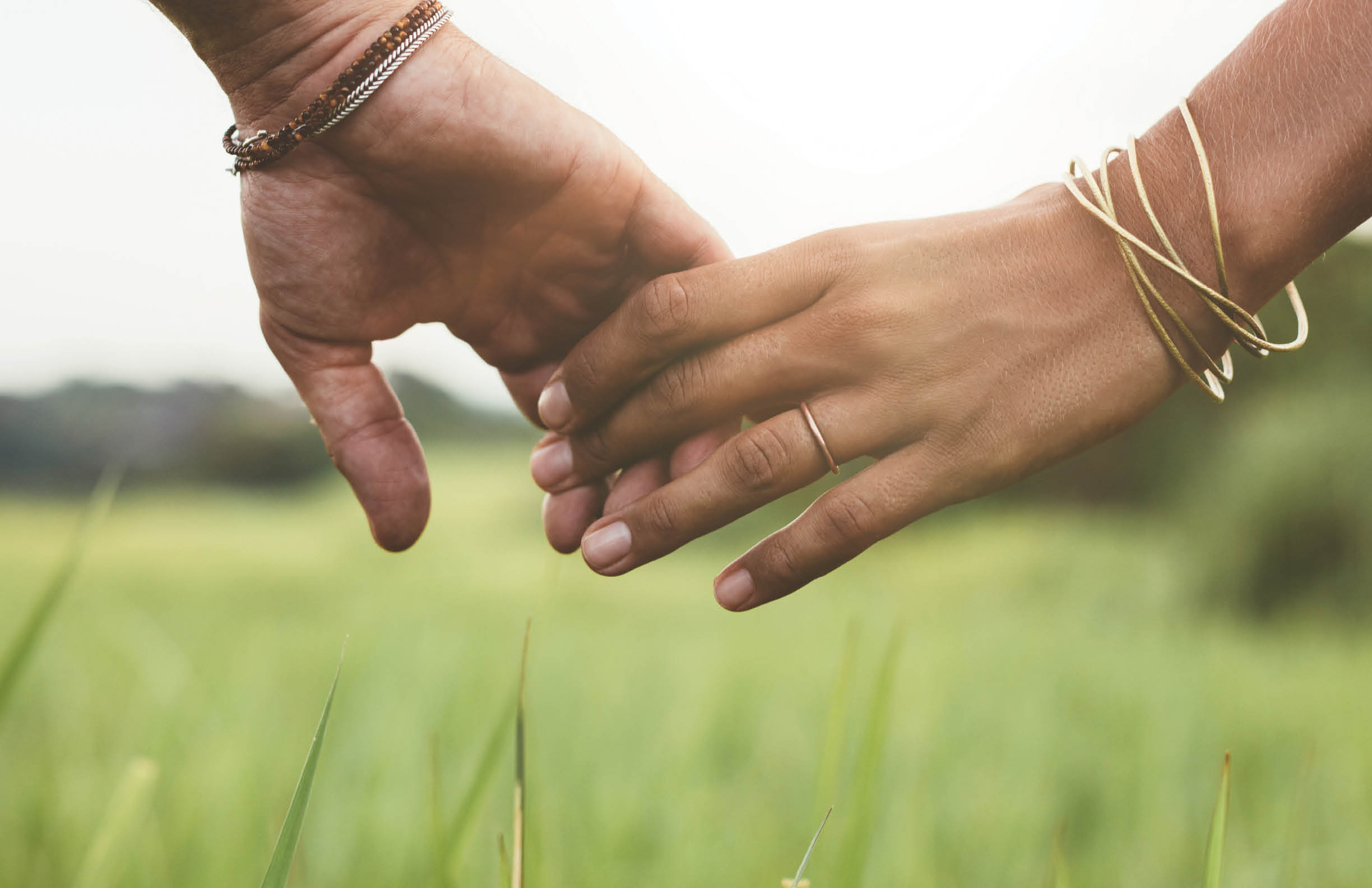 Horizontal shot of young couple walking through meadow holding hands with focus on hands .