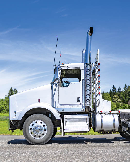 Industrial day cab big rig powerful white semi truck tractor with back protection wall and chrome parts transporting trees logs on special semi trailer running on the flat road in Columbia Gorge area