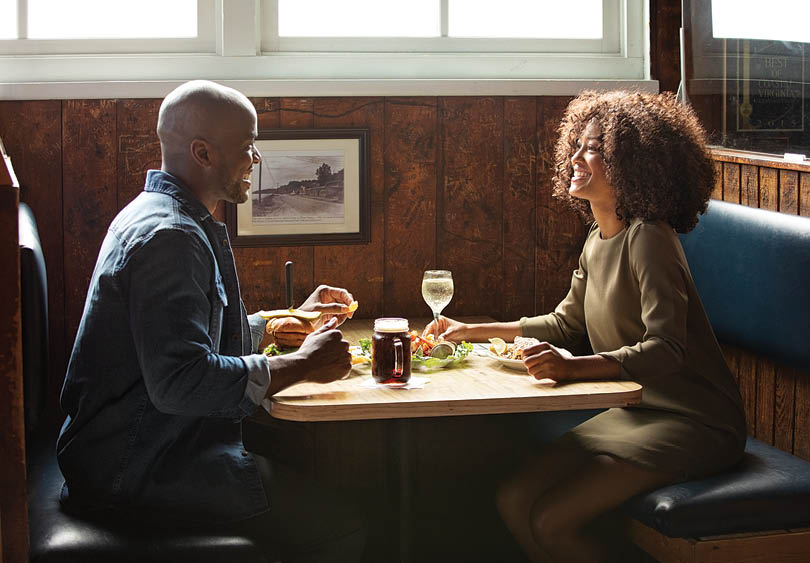 A man and woman sitting at a table with food and drinks. Description generated by AI
