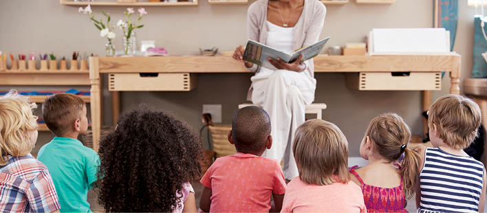 Teacher At Montessori School Reading To Children At Story Time