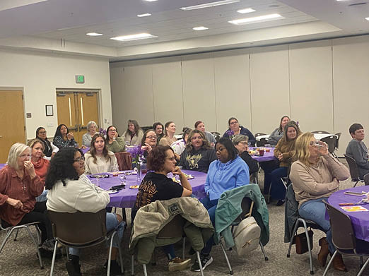 A group of women are sitting around a table, engaged in conversation. They are wearing glasses and are seated on chairs. The women are of various ages and are gathered in a room, possibly a classroom or a meeting space. AI generated content
