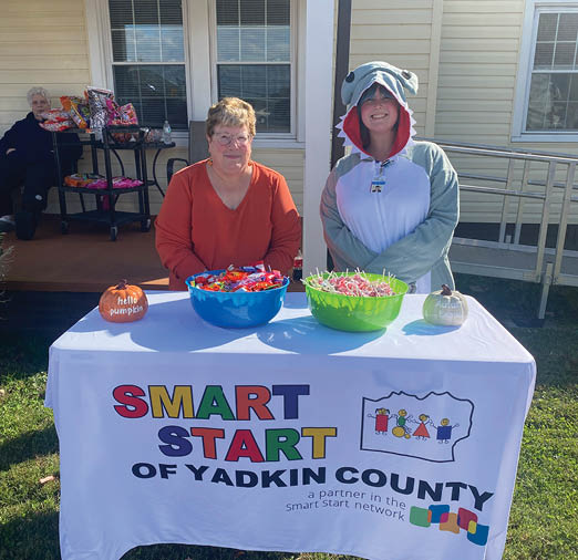 Two people are standing next to a table with a sign that says “Smart Start of Stark County." The table has a bowl of candy on it. AI generated content