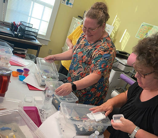 Two women are sitting at a table with plastic containers and crafts. AI generated content