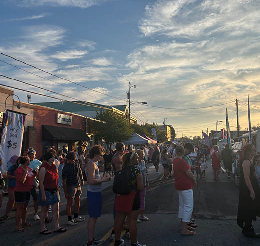 A large group of people are gathered on a street, some of them wearing red shirts. They are standing in front of a food truck, which is parked on the side of the road. The people are waiting in line to be served by the food truck. AI generated content