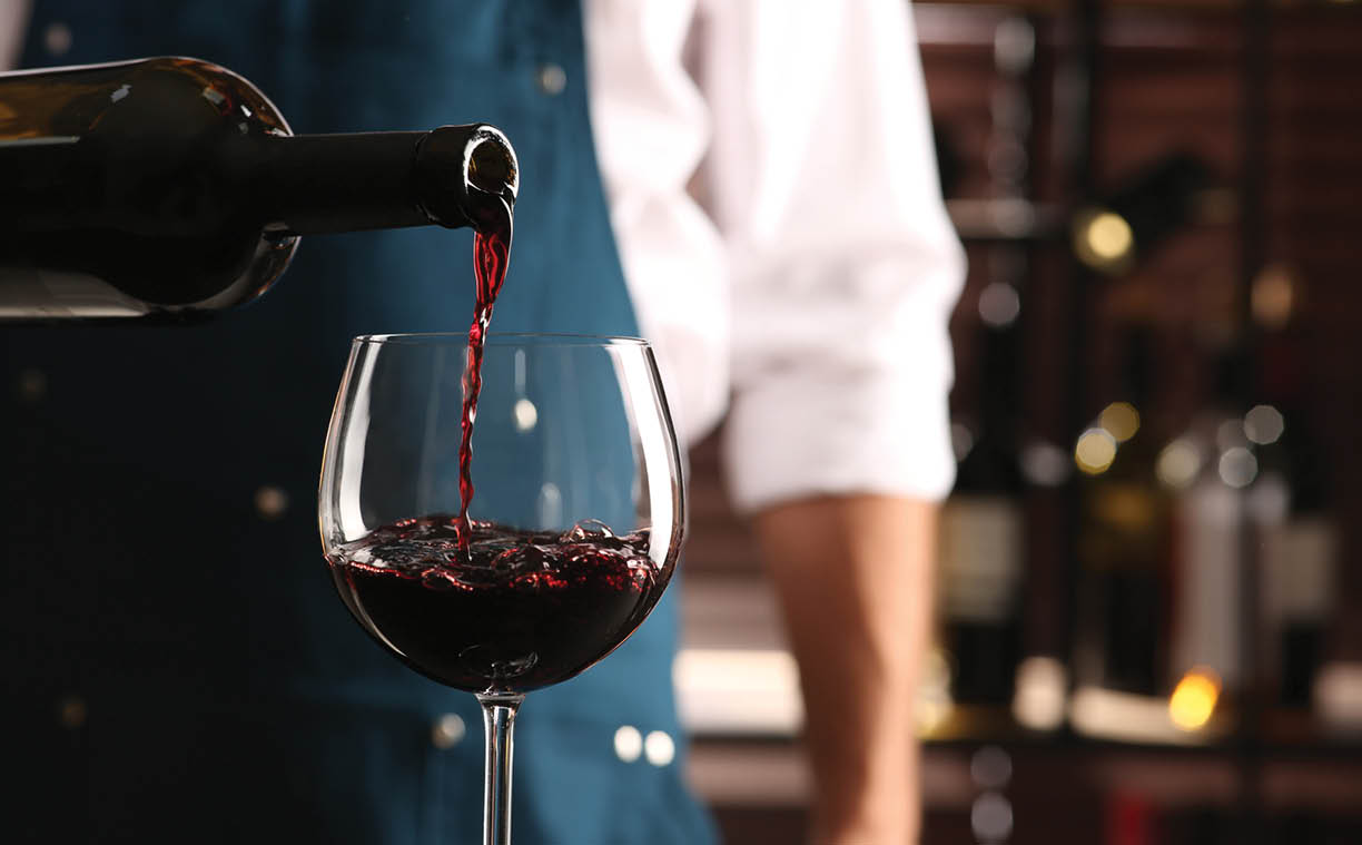 Bartender pouring red wine into glass indoors, closeup. Space for text