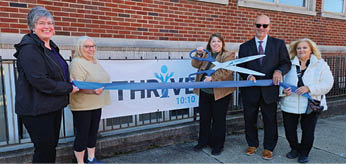 Four people are standing in front of a building, holding a pair of scissors and a ribbon. They are about to cut the ribbon, possibly for a grand opening or a special event. AI generated content