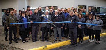 A group of people are standing in front of a building, posing for a picture. They are wearing suits and ties, and some are holding a blue ribbon. AI generated content