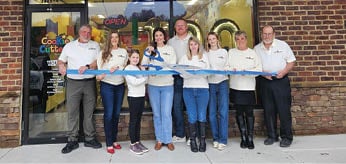 A group of people, including both men and women, are standing outside a hair salon. They are posing for a picture, and some of them are holding a blue object. AI generated content