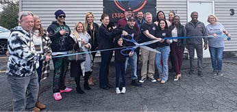 A group of people are standing in front of a building, posing for a picture. They are holding a blue ribbon, which they are about to cut. AI generated content