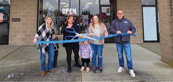 Four people are standing in front of a store, holding a blue ribbon. AI generated content
