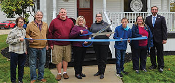 A group of people are standing in front of a building, posing for a picture. They are holding a ribbon and are about to cut it. AI generated content