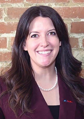 A woman wearing a maroon suit and a pearl necklace is smiling for the camera. AI generated content