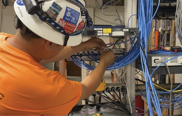 A man wearing a hard hat is working on a network of wires. AI generated content
