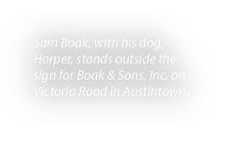 Sam Boak, with his dog, Harper, stands outside the sign for Boak & Sons, Inc. on Victoria Road in Austintown.
