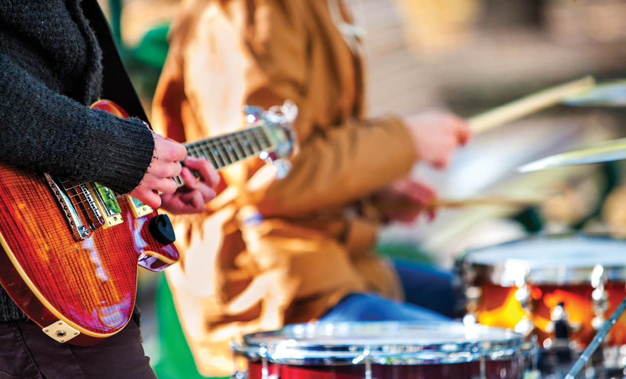 A man is playing a guitar while another person is playing drums. Description generated by AI