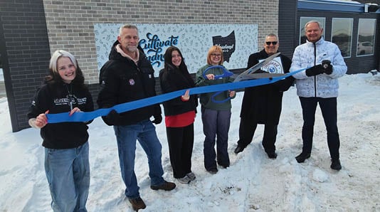 A group of people standing in the snow, holding a blue ribbon. Description generated by AI