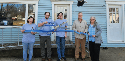 A group of people are cutting a blue ribbon in front of a building. Description generated by AI