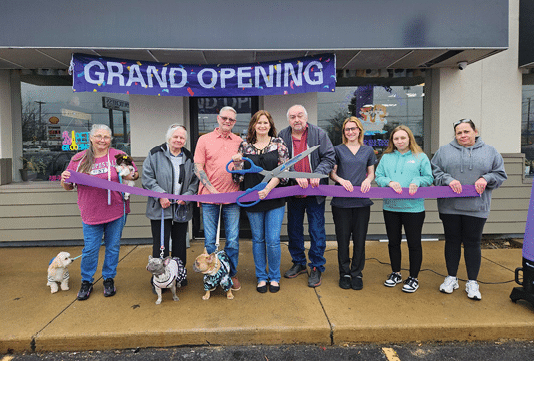 A group of people are standing in front of a building with a purple ribbon. Description generated by AI