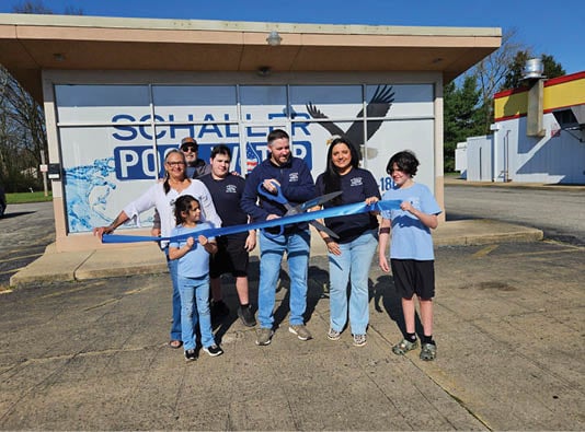 A group of people standing in front of a building with a blue ribbon. Description generated by AI