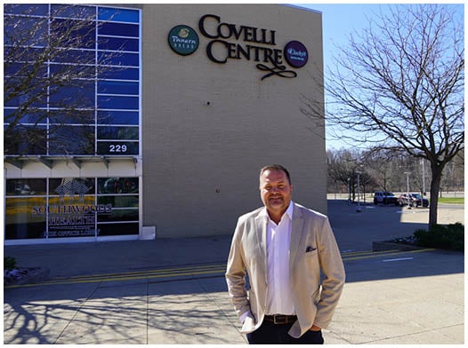 A man wearing a suit and tie standing in front of a large auditorium. Description generated by AI