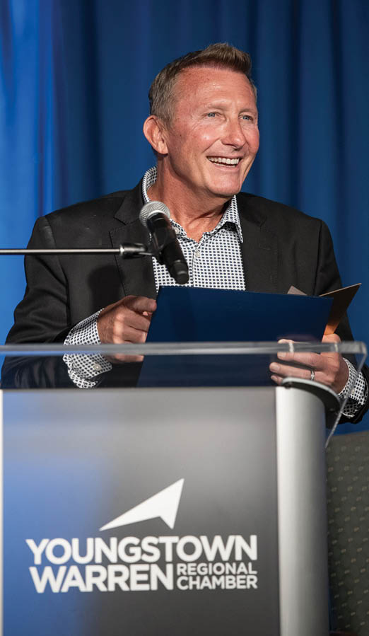 A man is standing at a podium holding a piece of paper. Description generated by AI