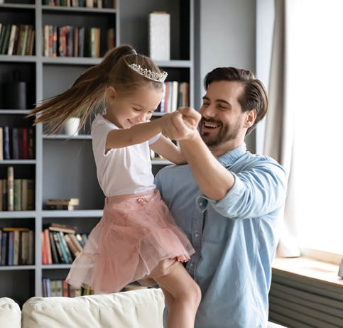 Overjoyed dad have fun with cute little preschooler daughter wearing crown and beautiful skirt, happy young father dancing with small excited girl child, listen to music playing at home together